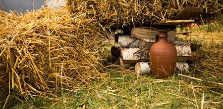 old traditional clay vase on a ground of fence village yard surrounded by stack hayの写真素材