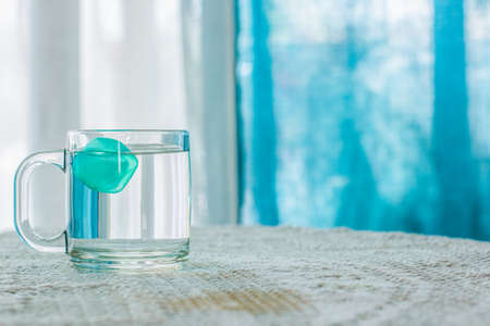 water with ice in cup on table white interior and blue curtains unfocused background, warm summer season concept photography, empty copy spaceの写真素材
