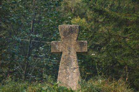 stone concrete cross religion sigh on ground hill with forest spruce needle trees dark green moody foliage unfocused background scenic view spaceの写真素材