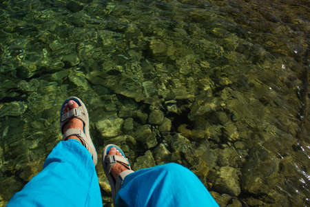 male feet in sandals above shallow water reservoir background scenic top view wallpaper empty copy...