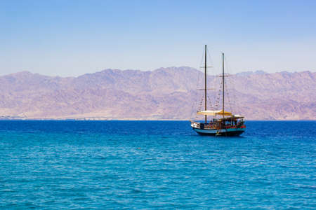 cruise tourism on a sea summer season scenic landscape picture of vintage wooden ship floating on water in Persian Guld near Saudi Arabia desert mountains waterfront viewの写真素材