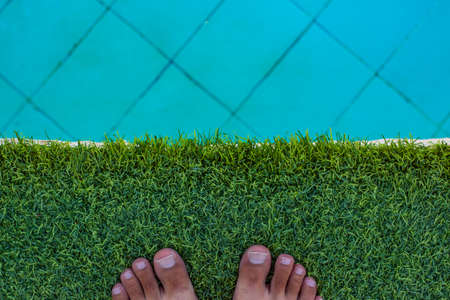 summer time vacation season swimming pool hotel relaxation space background with male bare feet on a synthetic grass floor, empty copy space for your textの写真素材
