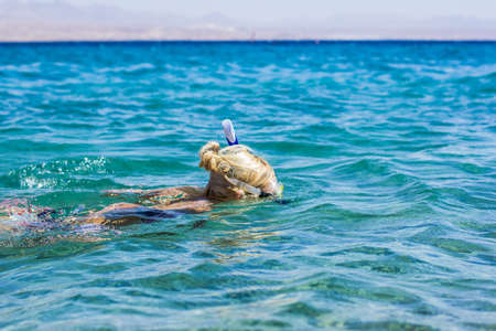 swimming snorkeling girl in Red sea blue water wavy surface in summer time vacation season outdoor...