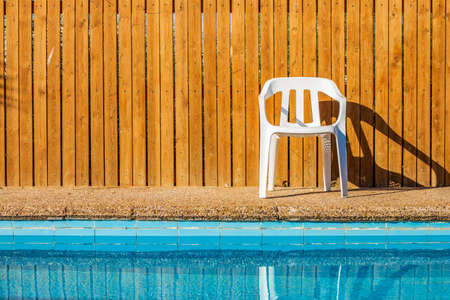 pool side relaxation space back yard blue water and wooden deck wall background with white chair simple symmetry wallpaper pattern picture with parallel lines summer time vacation seasonの写真素材