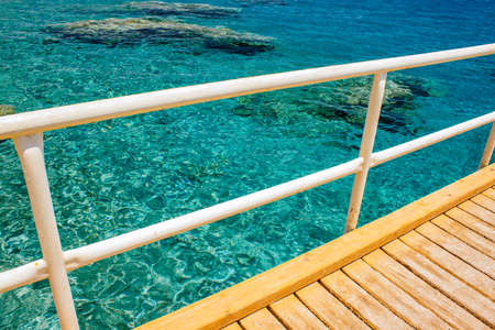 summer time wooden pier white pipe fence outdoor view from above on transparent water of Red sea with coral reefs on bottom copy spaceの写真素材