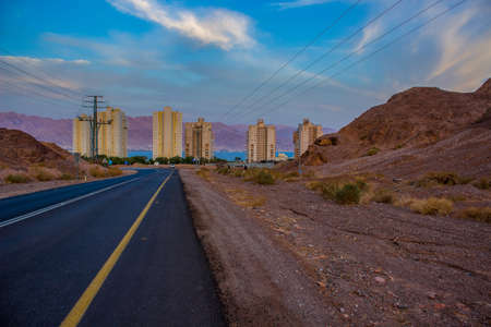 outskirts car road to Eilat Israeli city urban country side view with sand stone rocks foreground and living buildings background in soft colors twilight lighting eveningの写真素材
