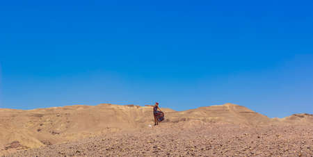 lonely woman person in fluttering dress desert landscape panoramic scenic view dry warming nature outdoor environment of Israel sand stone ground and blue sky background empty copy spaceの写真素材