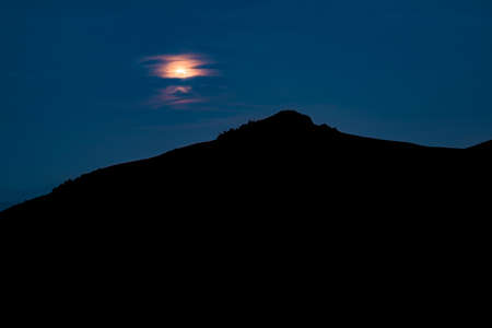 Black mountain silhouette time phantom blue night sky dark abstract landscape background wallpaper scenic view with unfocused moon behind clouds empty copy space for your textの写真素材