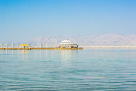 Dead sea health care Israeli resort destination Eastern site bridge to white gazebo building on waterfront coast line place in blue colors morning sun rise peaceful time outside environment copy spaceの写真素材