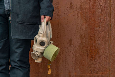 gas mask in hand of person in black coat rusty corrosion wall background industry dirty abandoned...