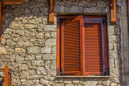 medieval wooden window frame with closed shutters on stone house wall background material texture...