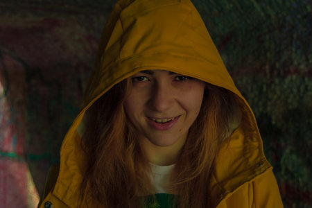 young girl scary smile Halloween concept face portrait in yellow rain coat hoodie twilight lighting...