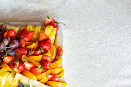 healthy food eating life style advertising poster concept picture of mixed fresh fruit plate with strawberry grapes and pineapple pieces top view on white table cloth background copy space for textの写真素材