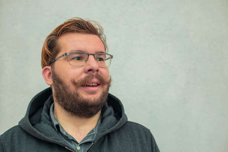smiling middle adult man with beard and glasses looking side ways in good mood, neutral white wall...