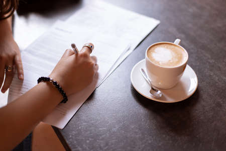 female hand sign model release document in cafe soft focus concept picture with wooden table and cup of coffeeの写真素材