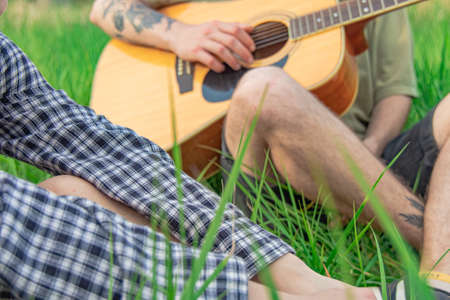 people company in nature with acoustic guitar incognito person without face in summer time bright clear weather day on green grass male body and feetの写真素材