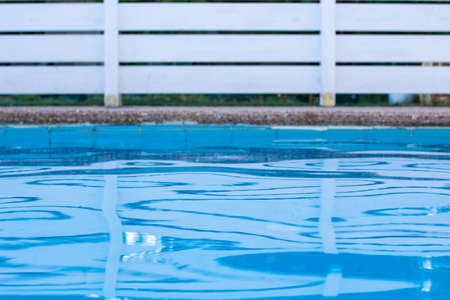 soft focus swimming pool side relaxation space blue water and garden white wooden deck fence background yard view copy spaceの写真素材