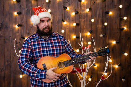 sad lonely man in Christmas time portrait with guitar in festive interior room wooden vintage wall...