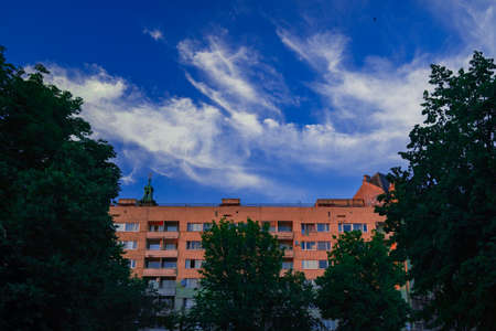 Eastern Europe country common apartment building exterior facade in frame of trees on cloudy blue sky background sceneryの写真素材