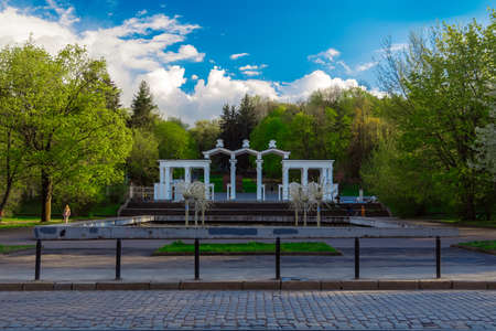 green park entrance square with marble architectural arch form and a lot of green trees foliage in clear weather dayの写真素材