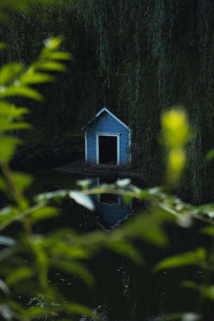 wooden bird feeder cabin landscaping object in park pond reservoir zone in dusk twilight lighting time with unfocused foliage vibrant color foreground vertical photoの写真素材
