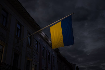 Ukraine independence day dramatic concept photography of Ukrainian flag yellow and blue color near government building on cloudy and stormy sky background symbolism of hard times in European countryの写真素材