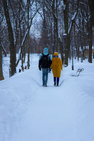 December winter park with a lot of snow, ordinary outdoor view, two person boy and girl walking with...