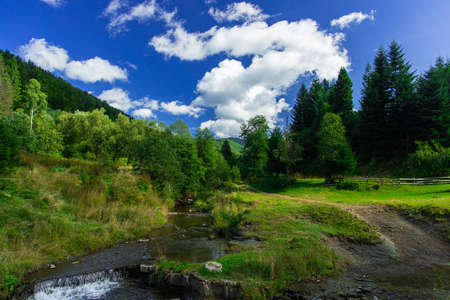 summer landscape if idyllic highland mountain valley with vibrant green color and white clouds on blue sky, beautiful natural place for hiking and walking on fresh air and environmentの写真素材