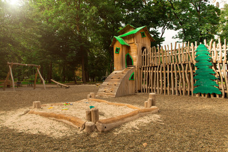 children playground area in landscape park with sandbox and wooden material castle carousel surrounded by trees, summer morning sun light warm natural viewの写真素材