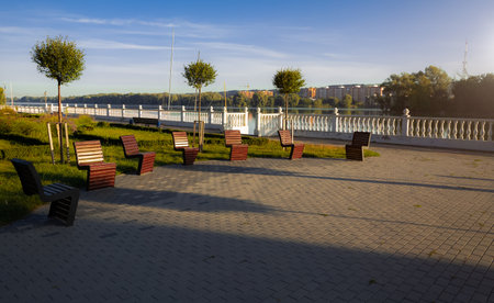 green city waterfront landscaped design pavement street coast district and wooden modern comfort chairs for rest outdoor space photography of morning warm sun rise timeの写真素材