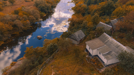aerial top view point country side outskirts cabin house near river shore line in woods with orange foliage in autumn October day timeの写真素材