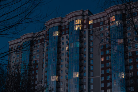 night city scape modern building architecture exterior facade windows illumination autumnal season time cause of bare branches trees foreground perspective viewの写真素材