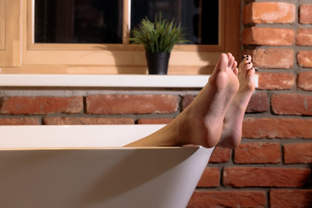 loft indoor bath room style brick walls background warm light and female body part intimate feet bare soles crossed legs foreshorteningの写真素材