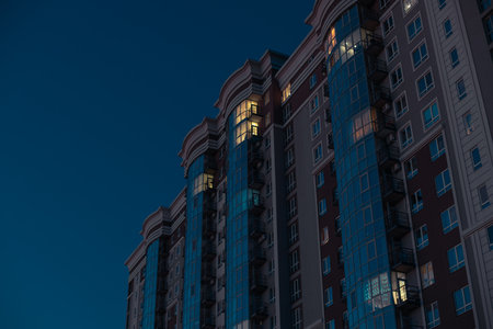 long exposure multi apartment living skyscraper building with design style glass facade and light illumination from windows in dark urban environment spaceの写真素材