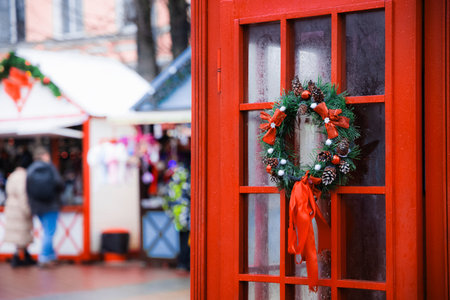 Classic red England telephone cabin with wreath on Christmas fair pedestrian market square place with foreground decorative elements and blurred background spaceの写真素材