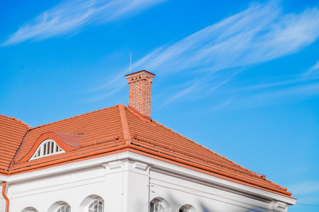cottage house white wall facade frame and roof red tile with chimney brick pipe shape on vivid blue...