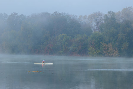 solitude peaceful water activity kayaking by person misty nature river and island trees seasonal foggy landscape background atmospheric environmentの写真素材