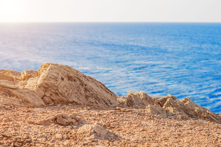 A rugged, sun-drenched cliff edge overlooks the vast, shimmering blue sea, evoking a sense of natural beauty and tranquilityの写真素材