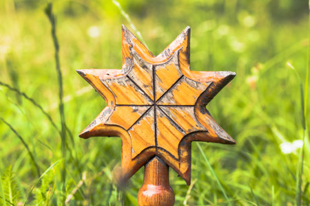 A handcrafted wooden star symbol, weathered and detailed, is placed outdoors amidst vibrant green...
