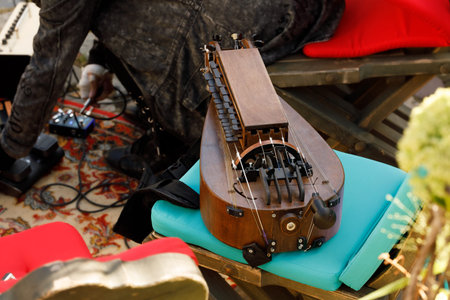 A detailed view of a wooden hurdy-gurdy resting on a turquoise cushion, surrounded by musical gear...