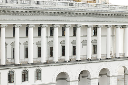 A grand white building showcases classical architecture with prominent ionic columns and repeating...