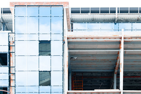 A partially completed modern building showcases a reflective glass exterior alongside raw concrete...
