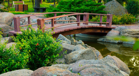 A picturesque garden scene featuring a charming wooden bridge, rocky landscape, and vibrant greenery...