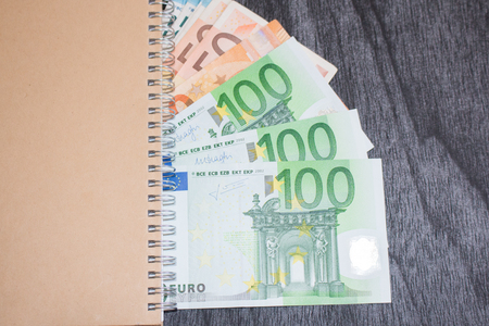 Notebook and money on the table. Notepad and euro banknotes on dark wooden background. Business and travel planning concept.の写真素材