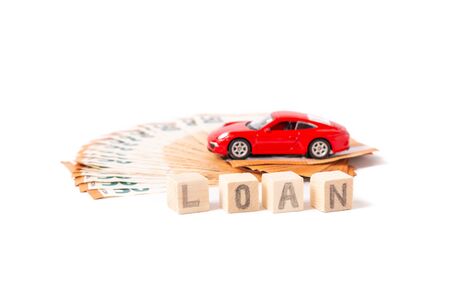 Finance and car loan, saving money for a car or material design concepts. Red car on euro banknotes. Money for car loan payment on white background. Wooden cubes with word loan. Copy space for text.の写真素材