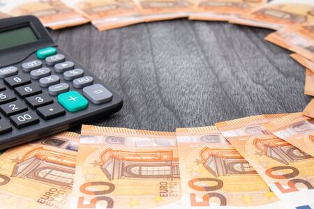 Calculator and euro money on grey wooden desk. Euro banknotes with black calculator on wooden...