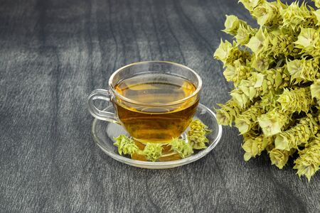 Greek traditional herbal tea in transparent cup. Bunch of mountain tea Malotira and mug with hot tea. Mountain tea sideritis. Natural Greek herbs on dark wooden background. の写真素材