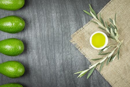 Healthy food concept. Fresh organic avocado, virgin olive oil and olive branches. Avocado with leafs on wooden table, top view, copy space. Natural ingredients.の写真素材