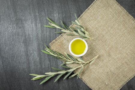 Top view of olive oil in a bowl, on wooden background. Olive oil with branches. Natural olive oil in white plate with branches around. Copy space for text or product.の写真素材