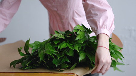 Female florist sorts out greens for a bouquet on kraft paperの写真素材